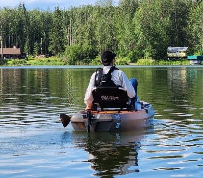 Allen paddling away from the shore in his kayak, across a still, tree-lined lake.
